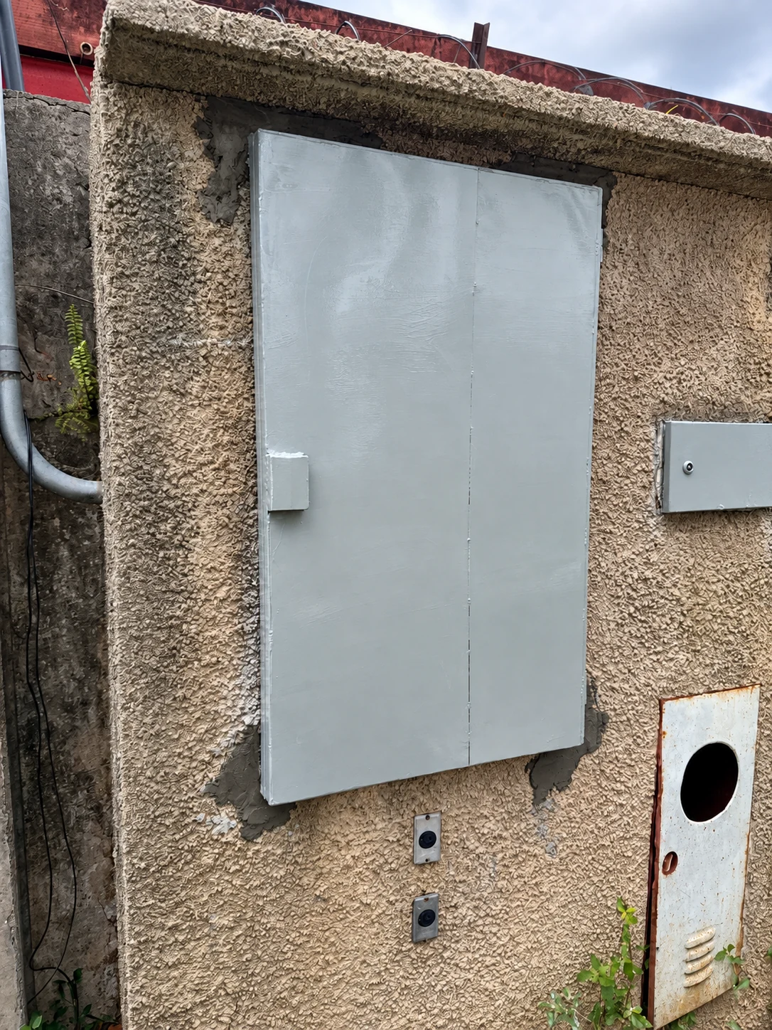 Porta de proteção instalada no acesso ao quadro, com estrutura e fechamento metálicos.